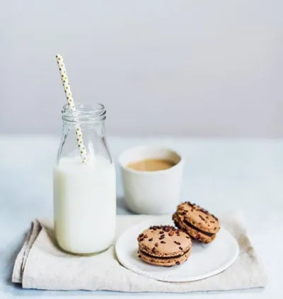 A glass bottle of milk with a straw next to chocolate sandwich cookies