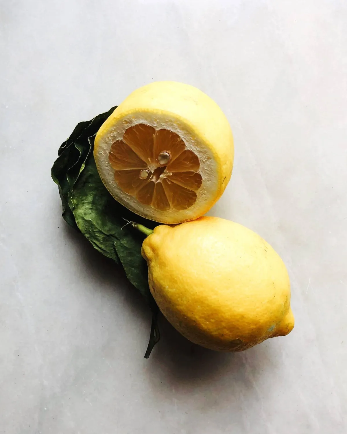 A whole lemon and a cut lemon with leaves on marble