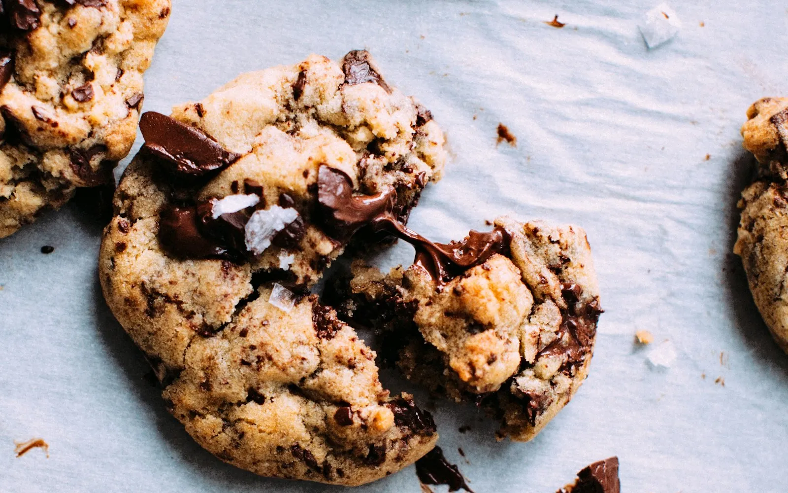 Thick chocolate chunk cookies with flaky salt on parchment paper